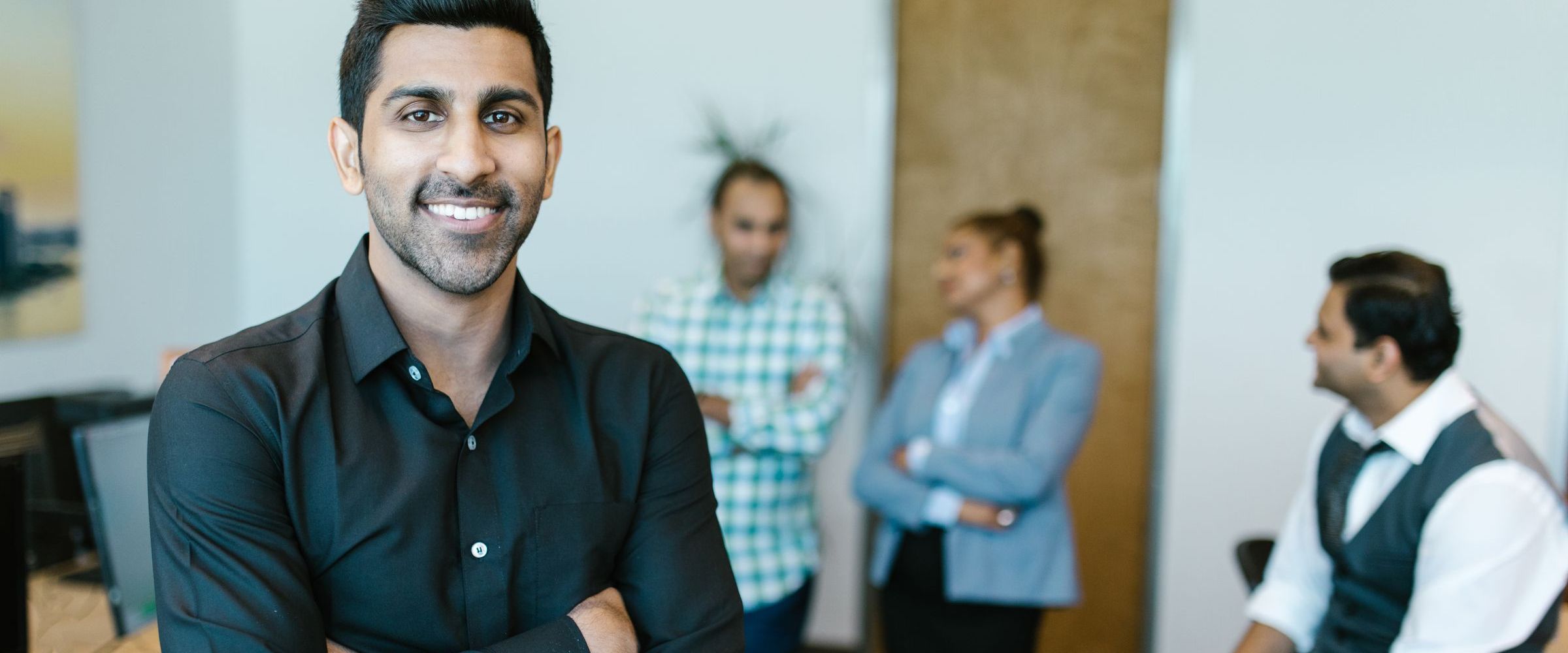 A smiling professional in an office with colleagues behind him
