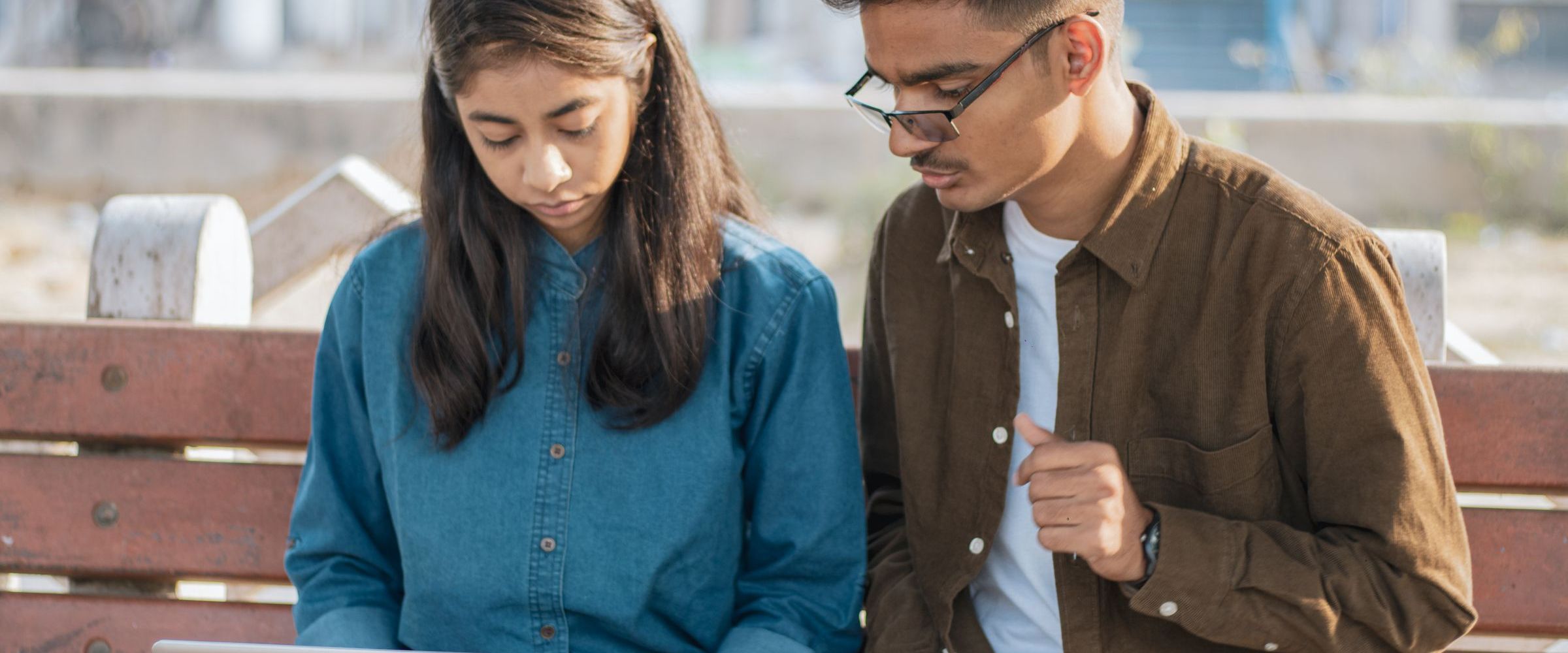 Two young people reading and discussing on a bench