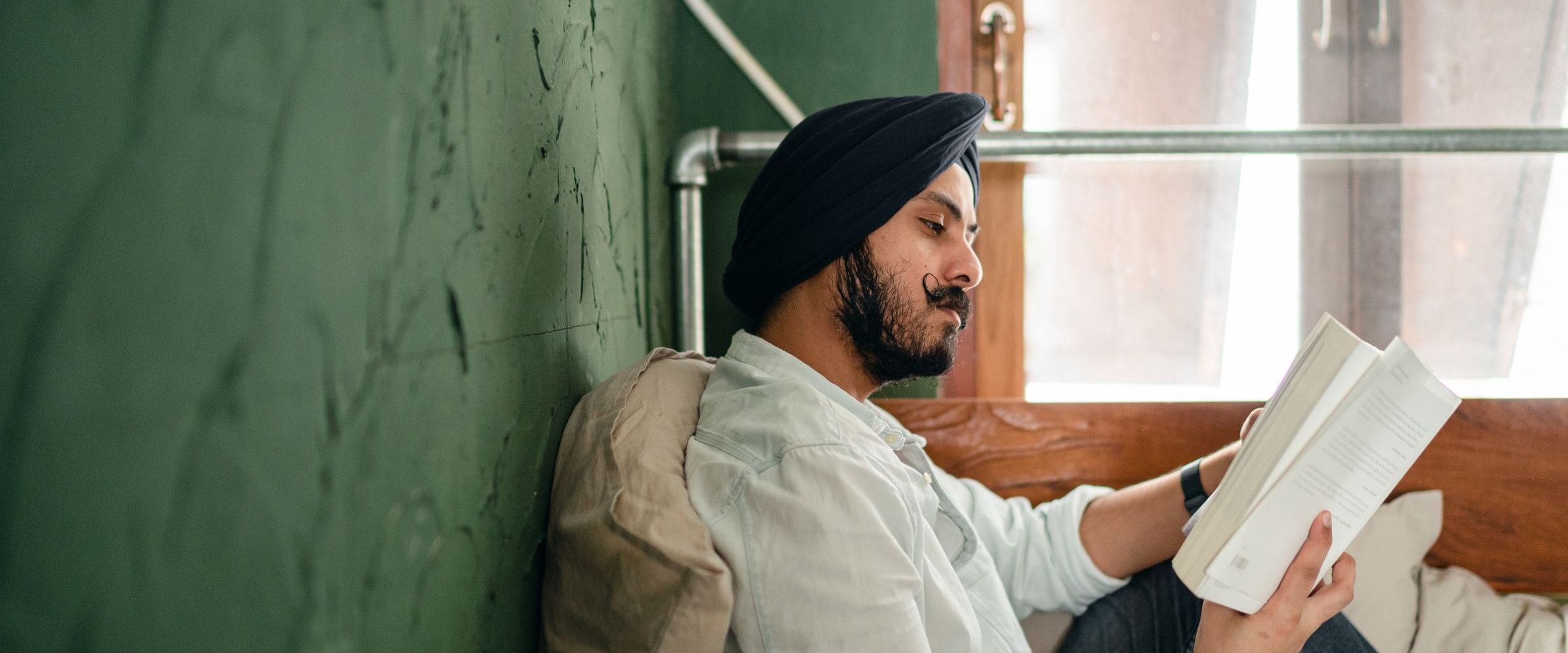 A man in a turban reading a book by a window